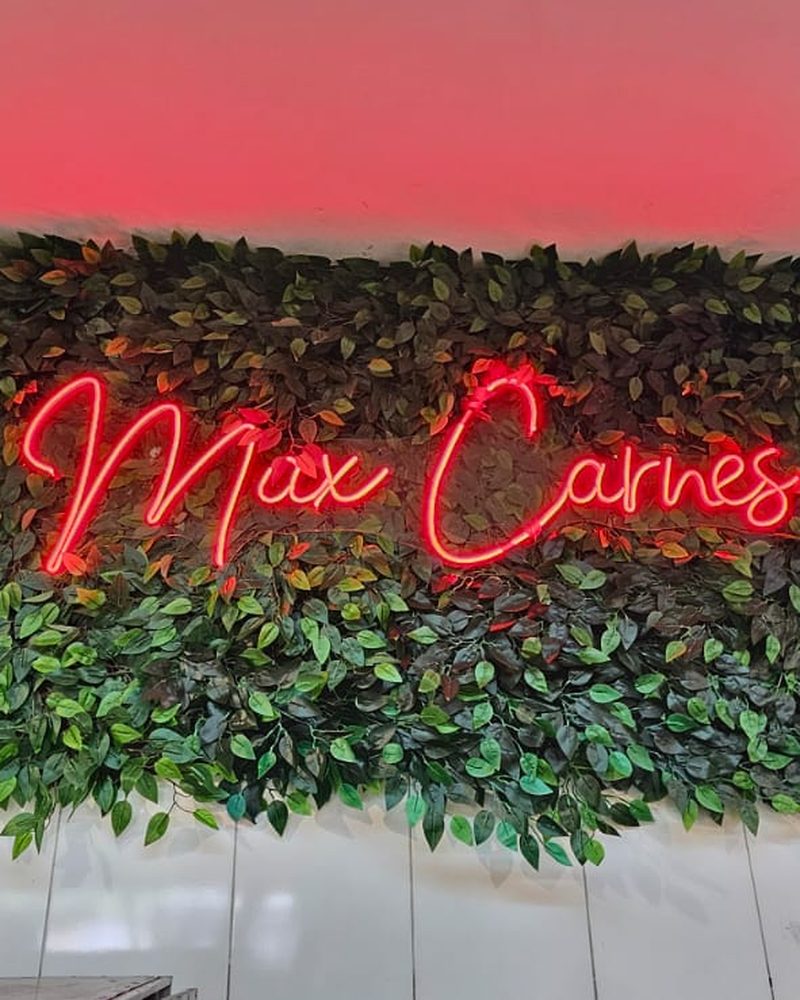 Parede de folhagem artificial com letreiro neon na Max Carnes